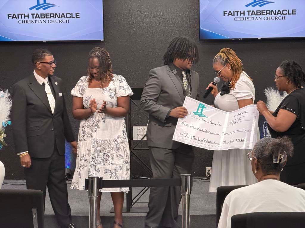 A church leader with a microphone congratulating a scholarship recipient holding his check