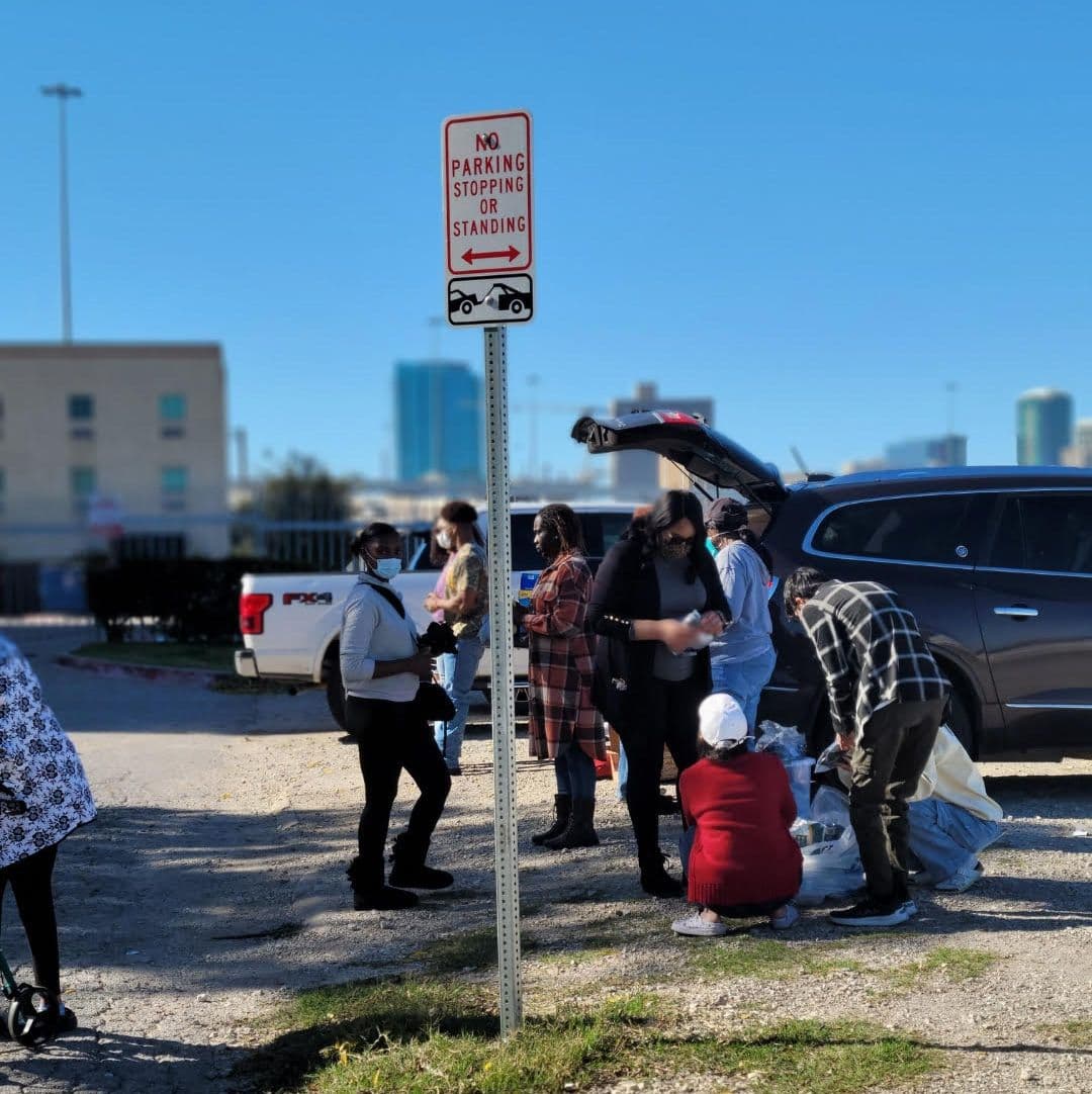 Volunteers kneeling to sort bags of donations beside a car during outreach