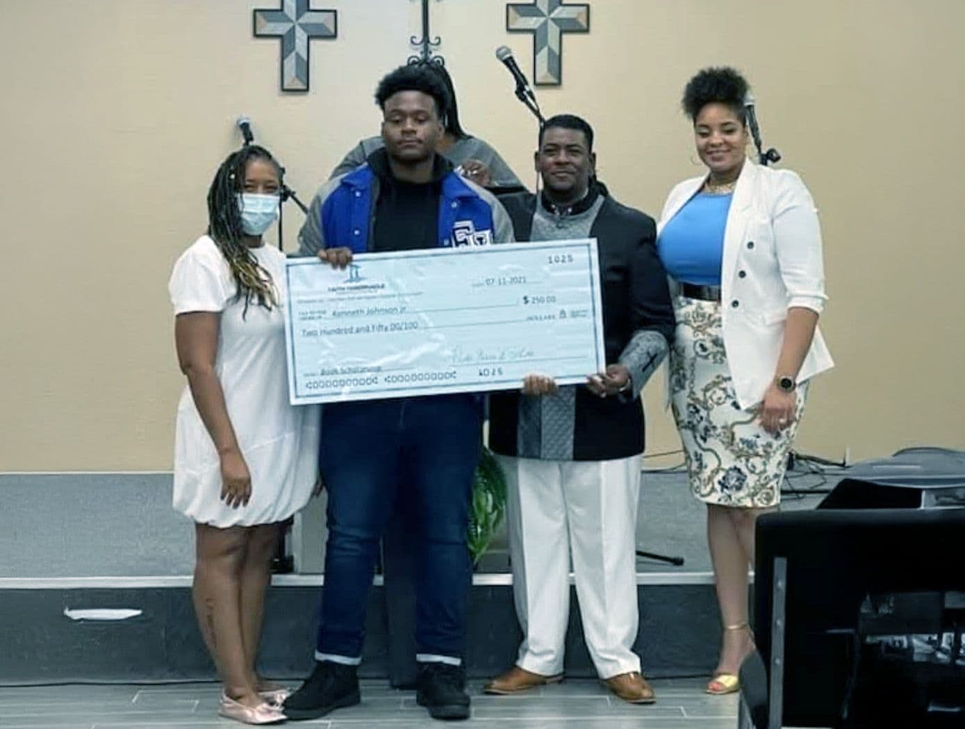A scholarship recipient in a letterman jacket holding his check with FTCC leaders in the sanctuary
