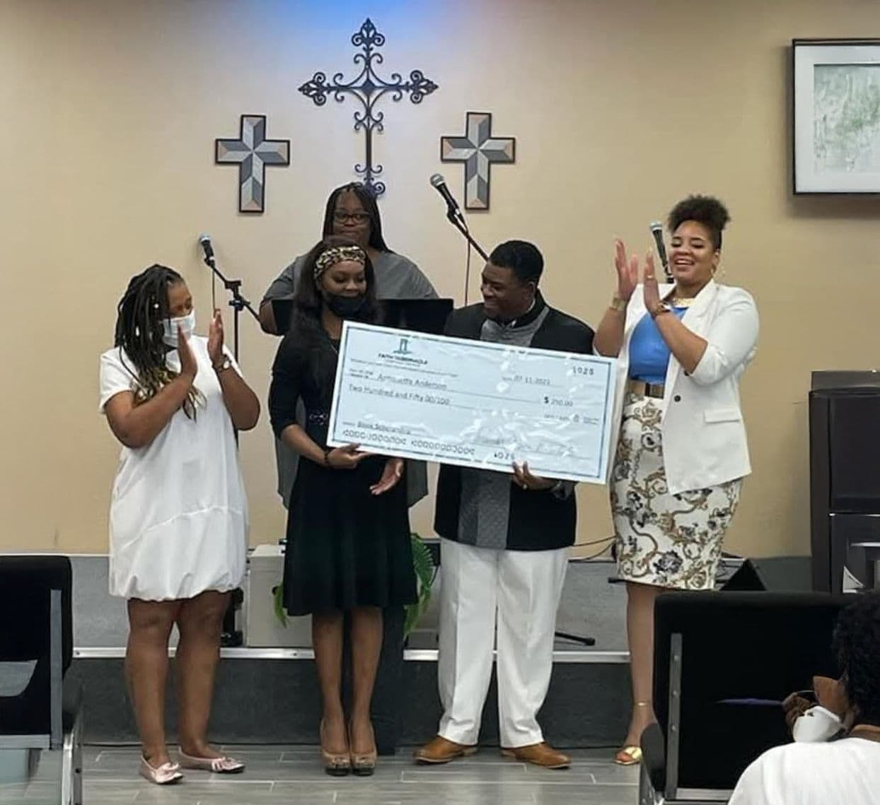 Church leaders applauding as a young woman receives her scholarship check